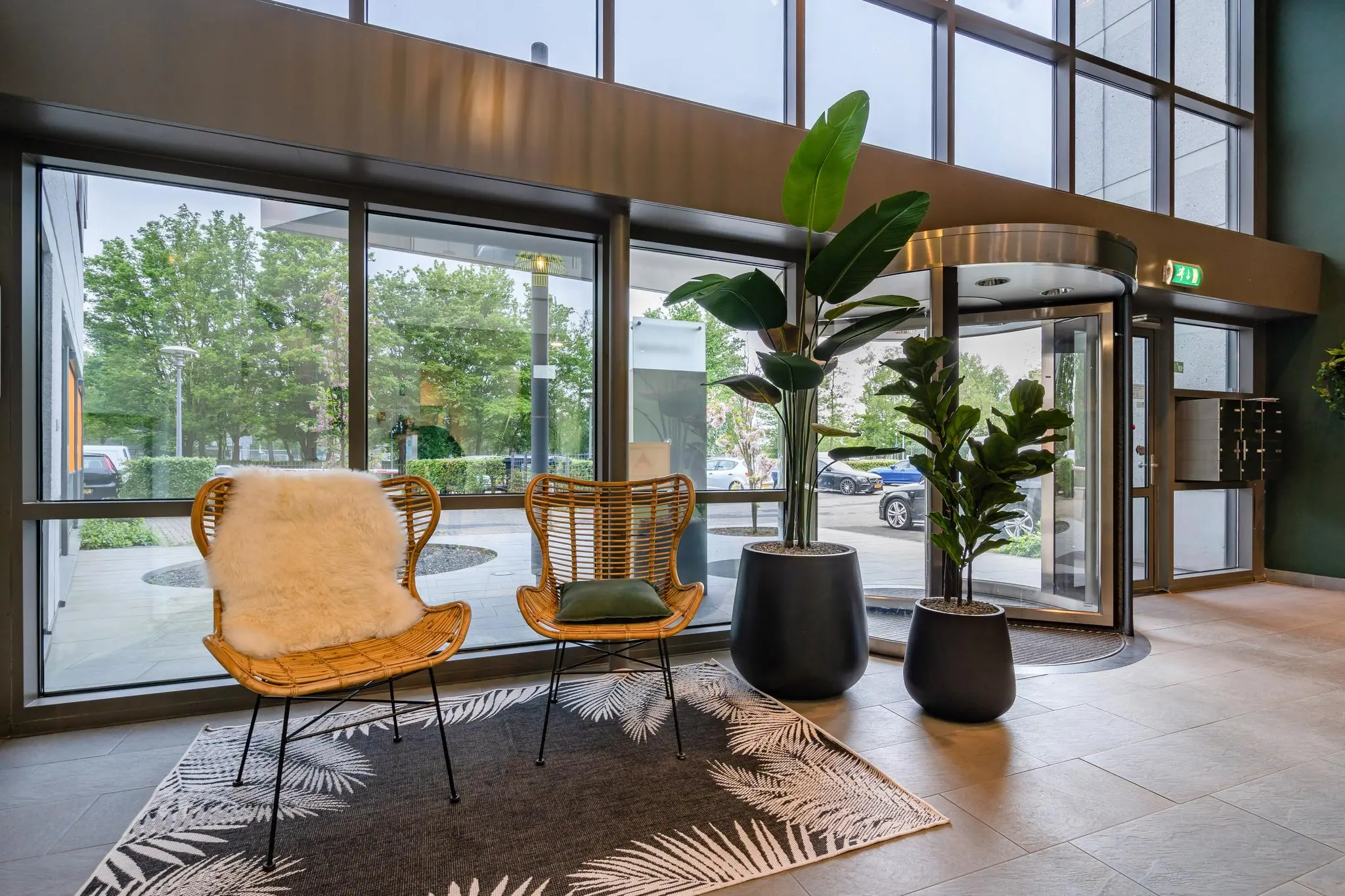 Moderne entree met rotan stoelen, grote planten en een draaideur aan de Baarnsche Dijk.